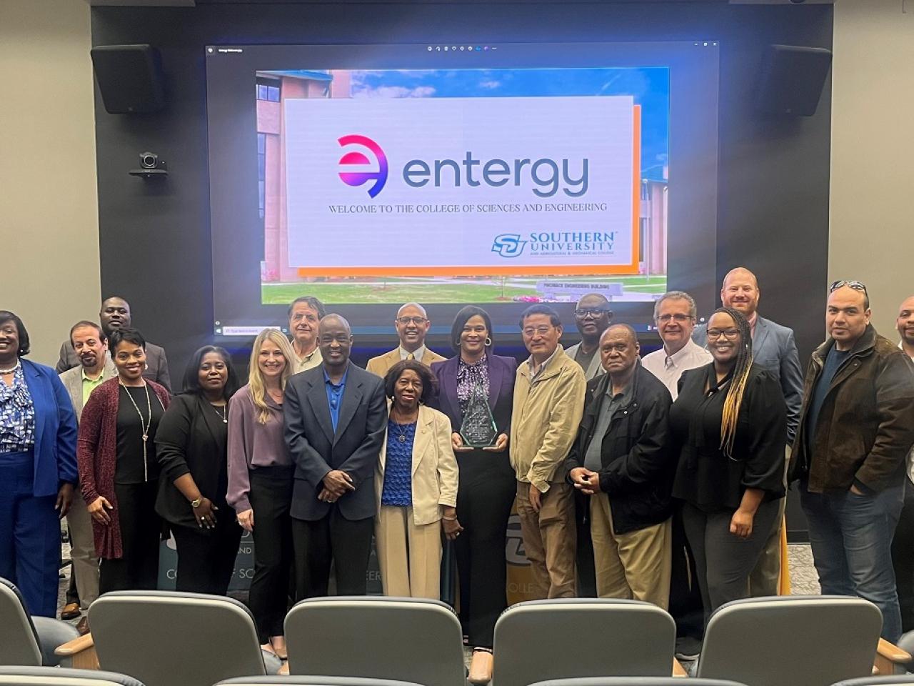 A group of people posed at the front of an auditorium. A digital display behind them with the entergy logo showing.