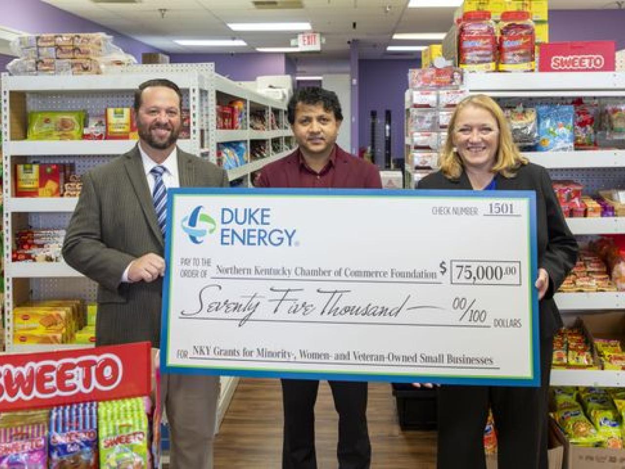 Three people in a small grocery store holding a large check.