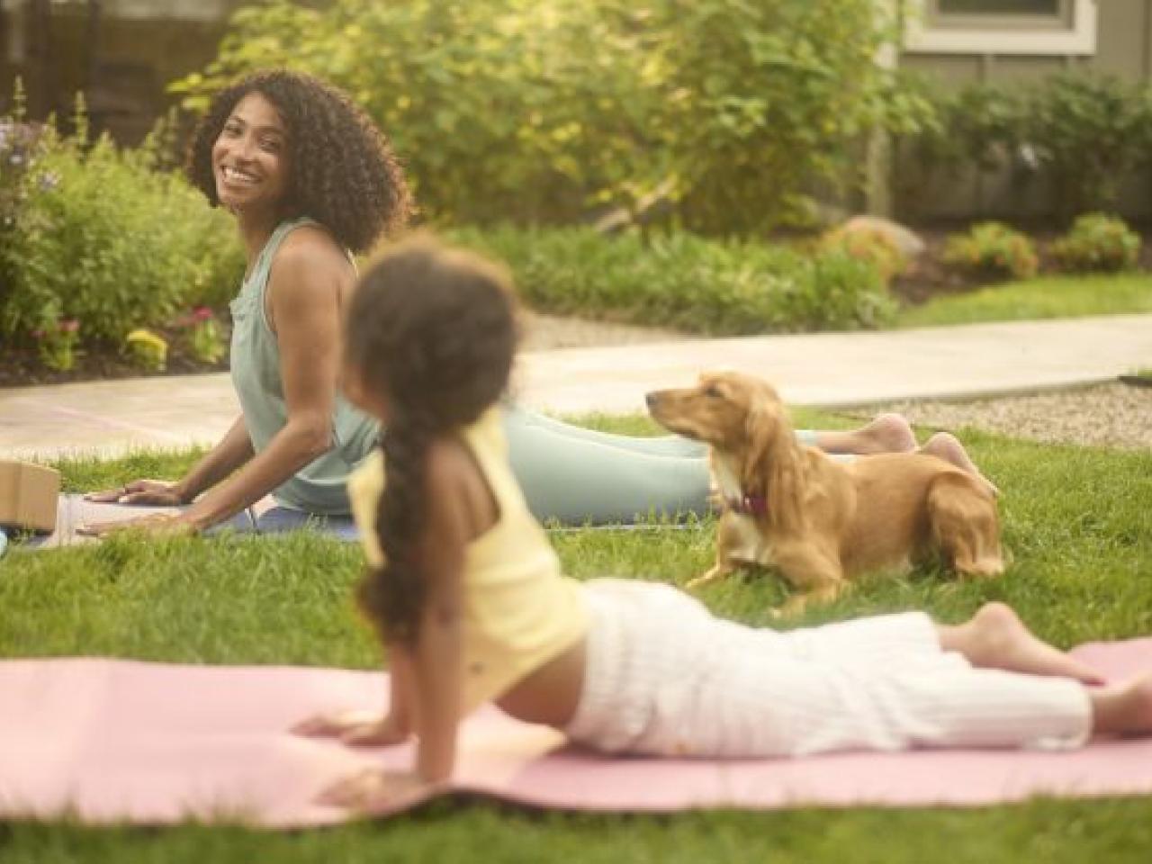 Adult and child doing yoga on a lawn with a dog nearby