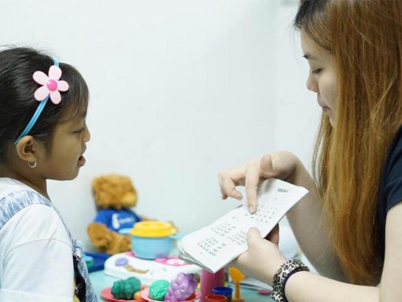 A caregiver works one-on-one with a young child during a speech therapy session.