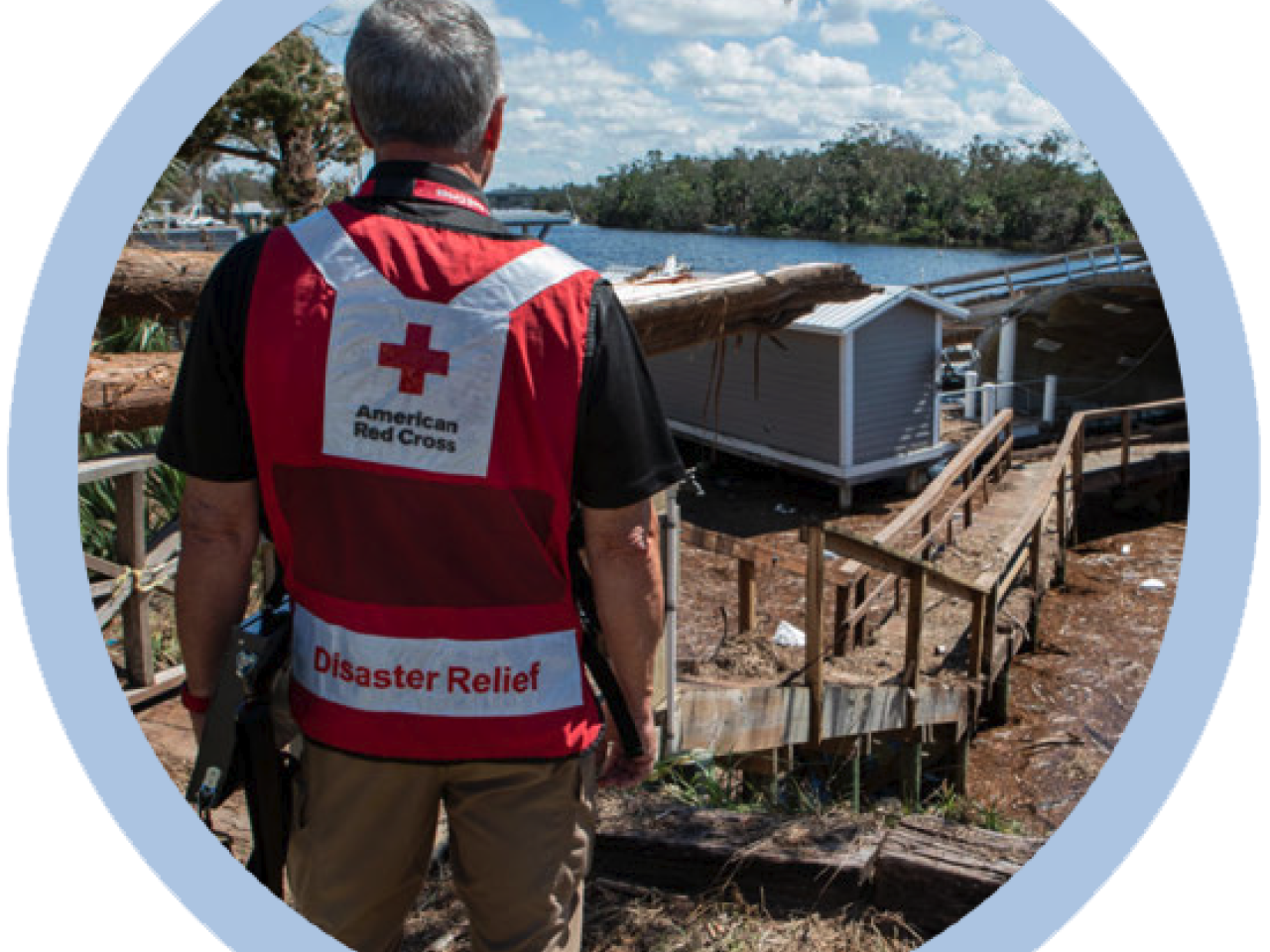 A person in a Red Cross Disaster Relief vest, looking out at damage
