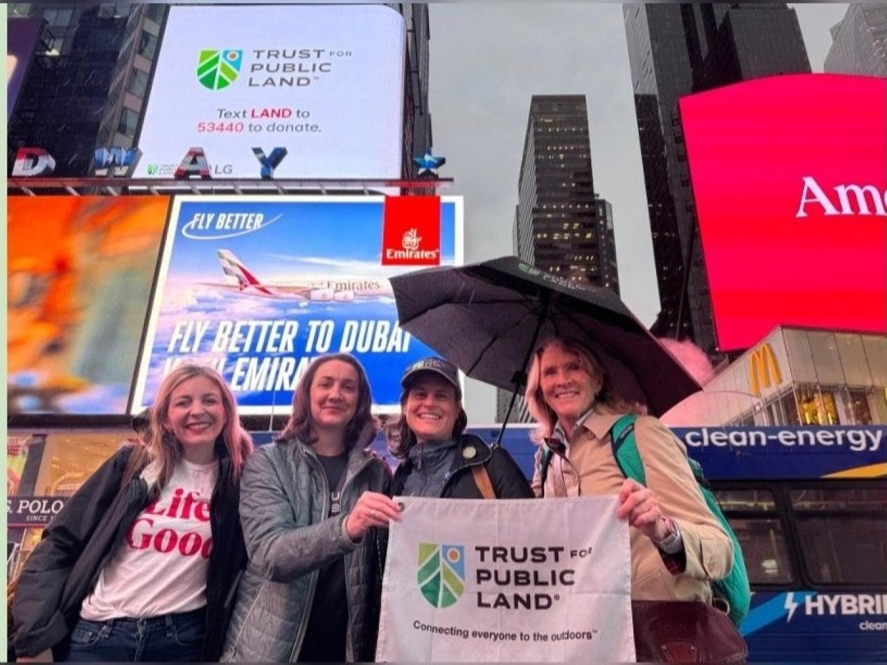 Four people together, holding up a sign that says "Trust for Public Land"