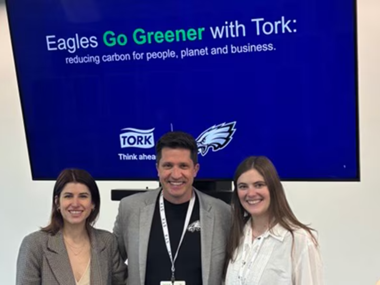 Three people standing in front of presentation. Screen behind says, "Eagles Go Greener with Tork"