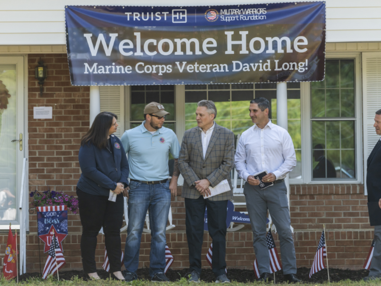 Sgt. David Long and three others stand outside his new home, a banner above them "Welcome Home"