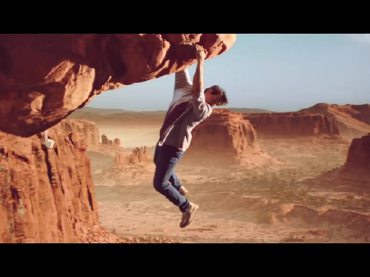 man hanging from mountainous rockface looking down