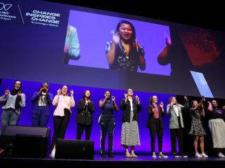 11 people standing in a row on stage.