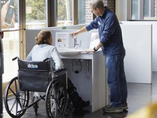 Woman in wheelchair being shown an accessible sink by a standing man