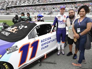 Mayra Hernandez, Jesse Iniguez and Denny Hamlin stand next to the FedEx 11 race car
