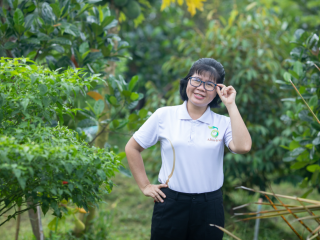 Nguyen Thi Kim Thoa standing in an orchard, touching the side of her glasses. Wearing an Abavina logo shirt