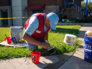Photo of man sitting in a patch of grass, painting a sidewalk