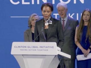 Didi Bertrand Farmer at a podium, The Clintons behind her.