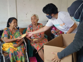 Two volunteers handing out food to two elderly people in chairs
