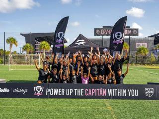 A soccer team posing with arms raised. Team banners in front and back sides "Power up the Capitan within you."