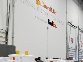 Large bay doors, "DirectRelief Global Distribution Center sponsored by FedEx" on the wall.