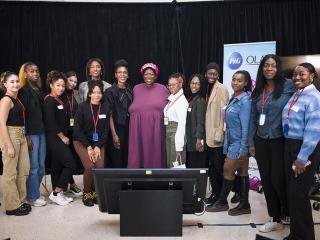 A group of women on a stage with black curtains behind. A floor monitor in front of them