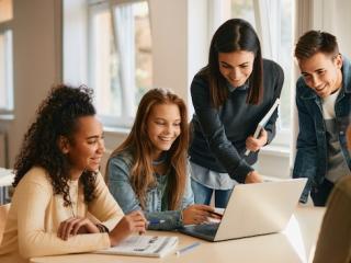 Teacher working with a group of four students who are seated behind a laptop.