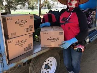 A worker holding a box with "always" logo, other boxes on an open cart next to them