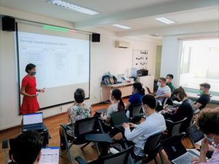 one person stands in front of a small classroom in front of a screen with a presentation being projected on it
