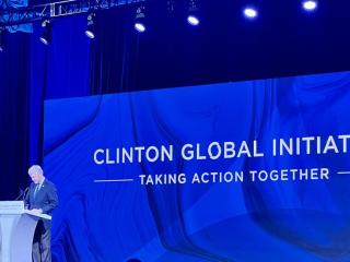 Bill Clinton at a podium, a large screen with "Clinton Global Initiative" behind him