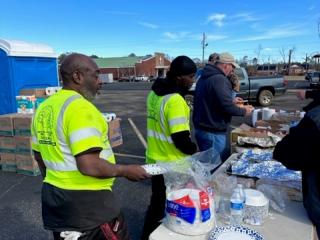 People in line being served food in a parking lot.