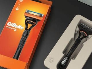 An orange box with Gillette logo and picture on a razor, on the right the product in a cardboard holding box.