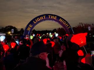 "We light the night" banner, red lanterns held by a group of participants at a nighttime event.