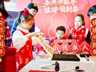 children watch as one lifts a piece of paper off an ink block. Signs in Chinese behind them and to the sides.