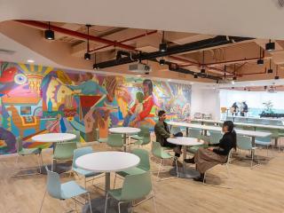 Two people at a circular table in a cafeteria type setting, a colorful mural on one wall.