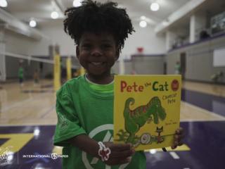 in a gym, a child with a big smile shows a book