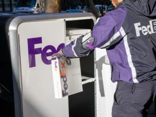 A person in FedEx uniform opening a tall cart with FedEx Express logo on it and pulling out a package.