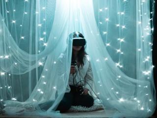 A person using a VR headset and controllers, sheer drapes and string lights around them.