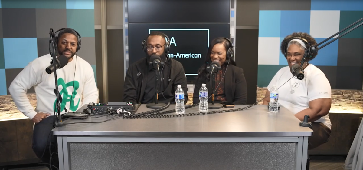 Four people with headsets and microphones, sitting at a desk.