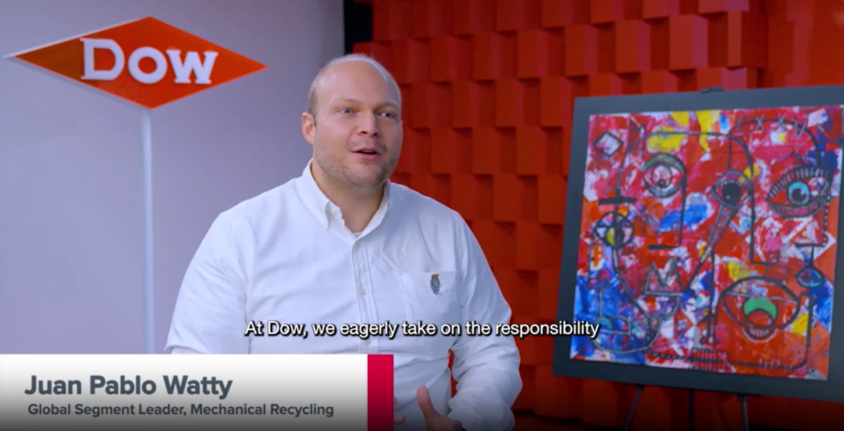 Juan Pablo Watty, seated for an interview. A White wall with Dow logo behind them, a red textured wall and painting on the right.