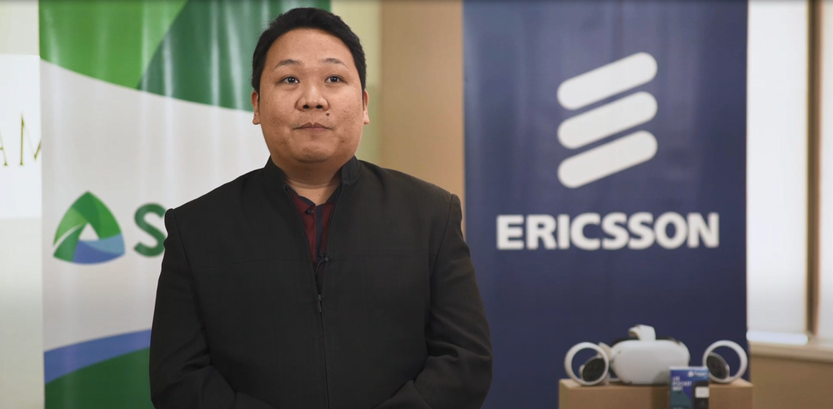 Dr. Bert Tuga sitting in front of an Ericsson sign, a VR headset to the right.