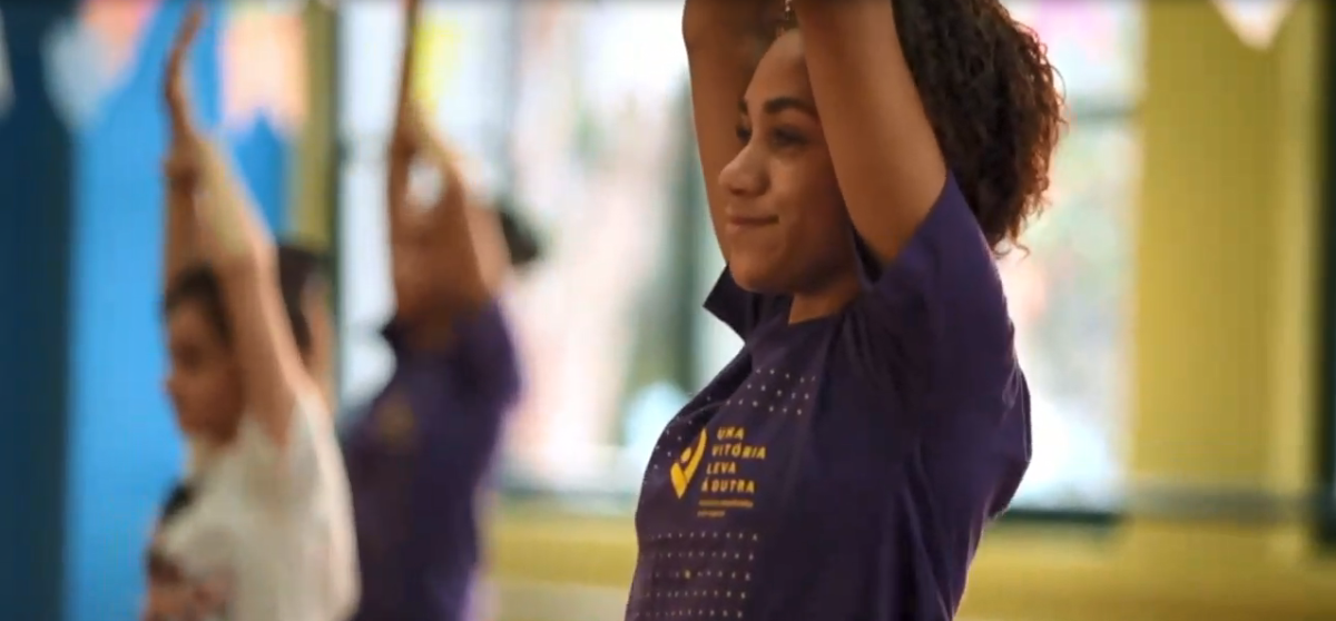 An athlete with both arms raised in a room with others doing the same in the background.