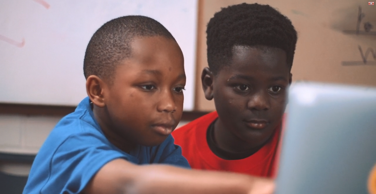 Two children looking at a laptop, one points to the screen.