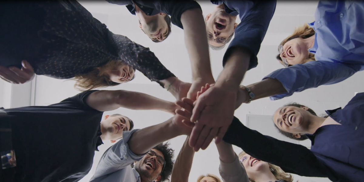 Looking up at a group of people each with a hand in the middle of a circle.