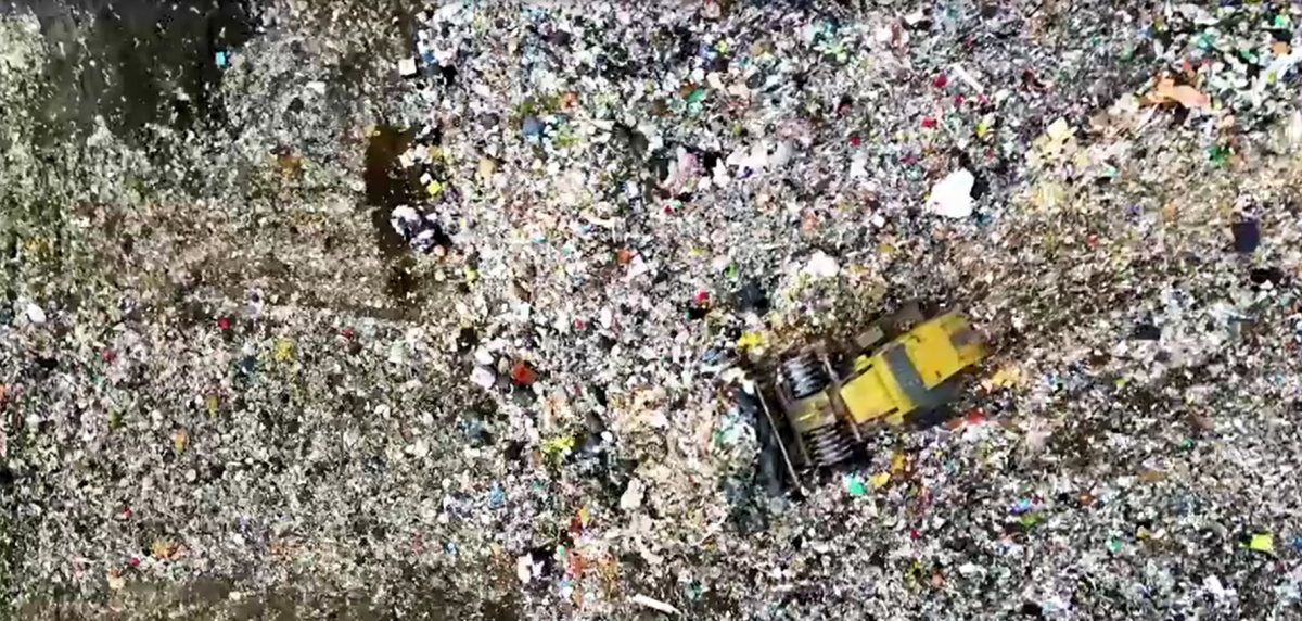 A bulldozer pushing piles of garbage in a dump.