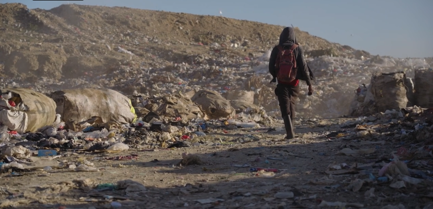 person walking away towards pile of garbage