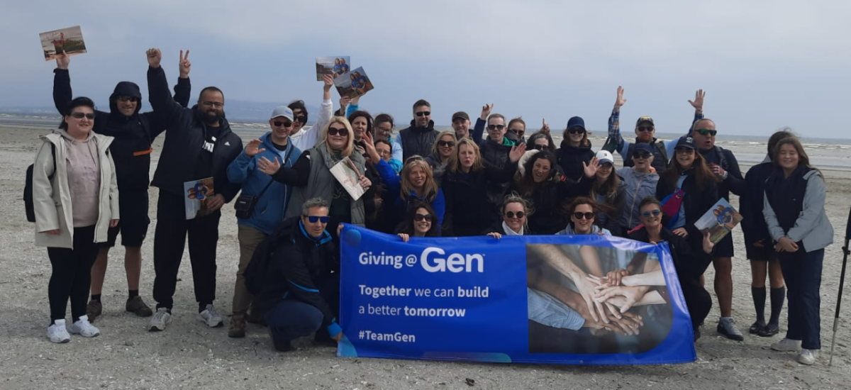 A group of people cheering on a beach, the front row holding a sign "Giving @ Gen".