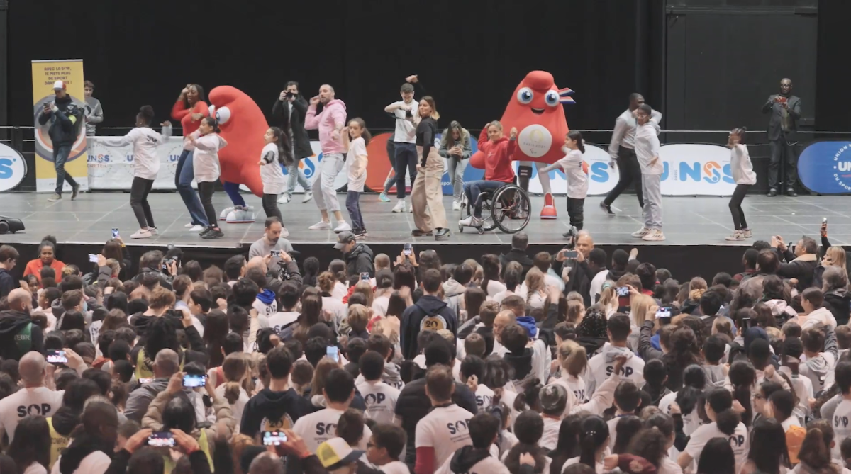 Adults and kids dancing on a stage in front of a crowd.