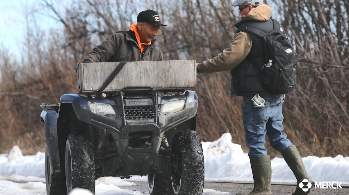 A person hand a package to another on an atv.