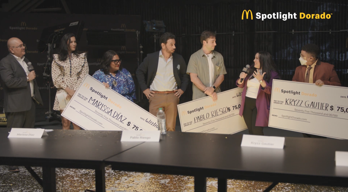 Three winners and presenters in a room each holding large checks.