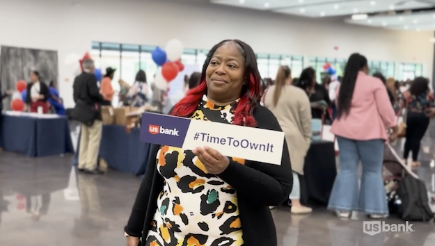 Melody Jones shown at a U.S. Bank location holding a sign that says "Time to Own It".