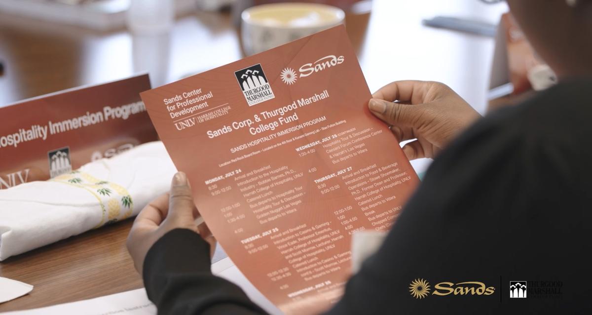 A person holding a schedule of events. Sands logo in the corner.