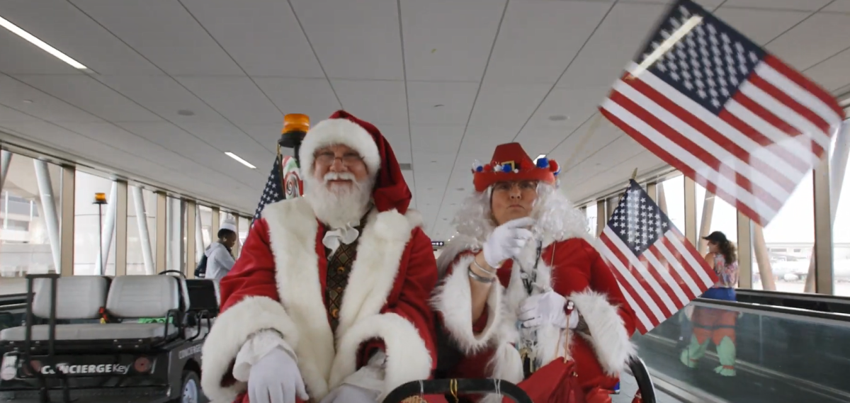 Santa and Mrs. Clause in an airport cart riding down an aisle waving american flags.