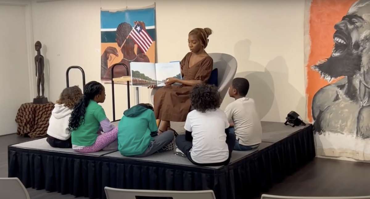 Children sat on the floor while a person shows them an illustrated book 