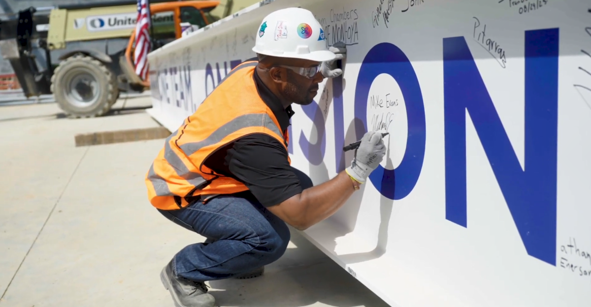 A person in hard hat and high-vis vest signs a large beam.