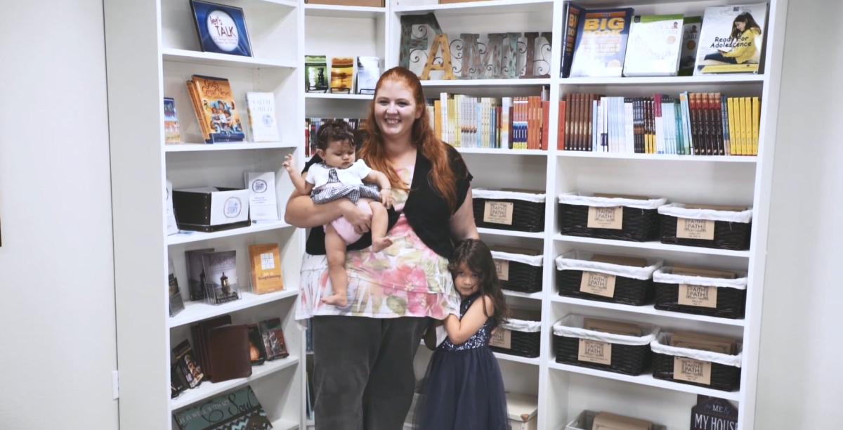 Michaela with two kids standing in front of a bookshelf.