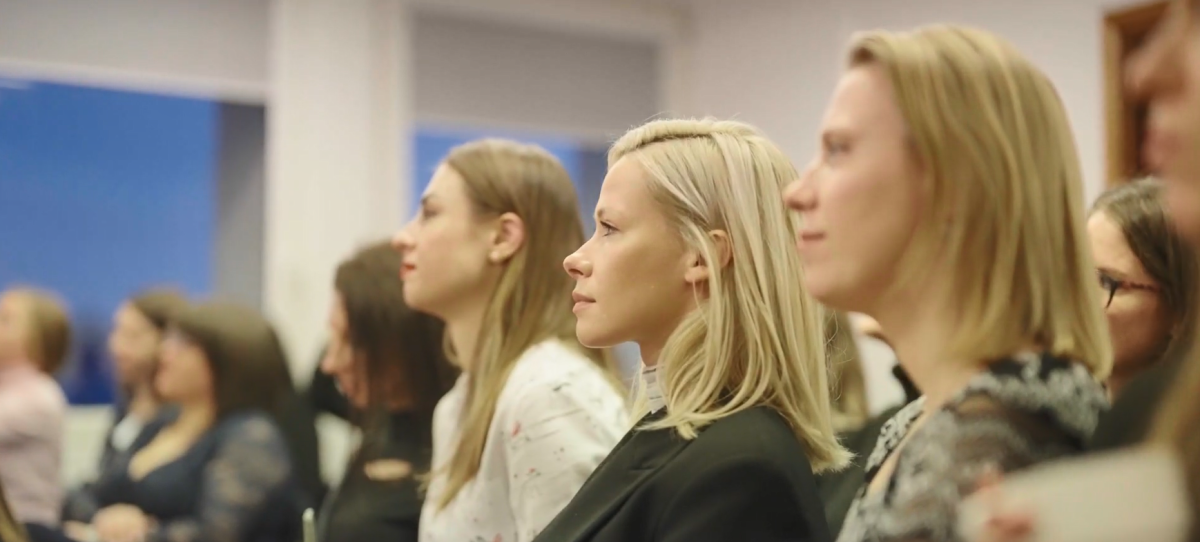 Seated people in a room of others, looking in the same direction.